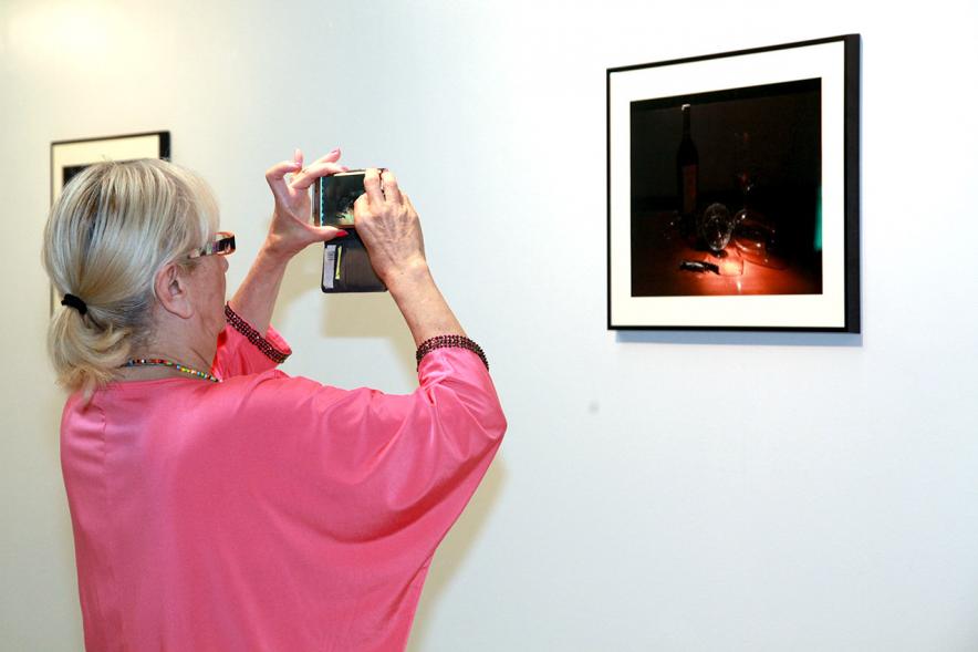 Inauguración Exposición "Objetos Iluminados" de A Contraluz - Imagen de persona haciendo una foto a una de las fotografías de la exposición.
