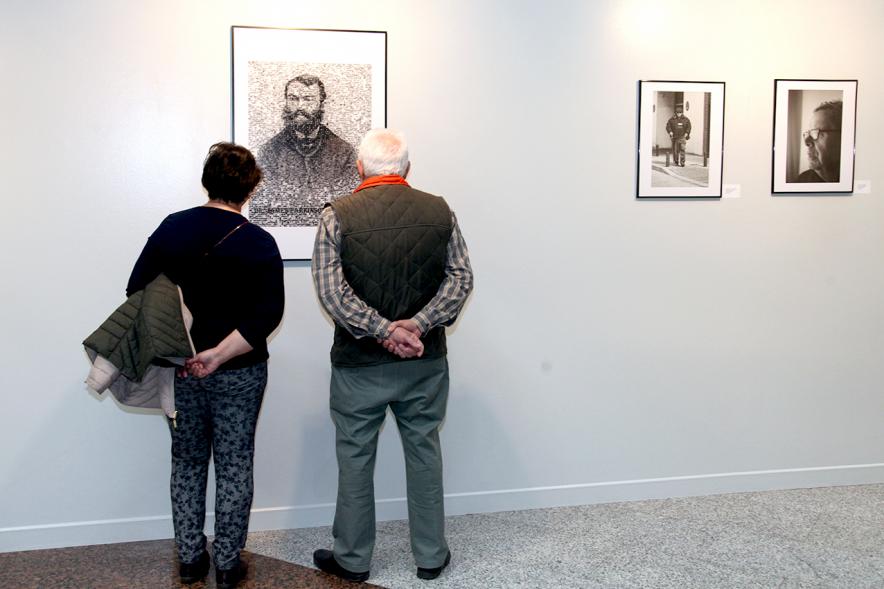 Inauguración Fotográfica sobre el Parkinson en el Patio de Encuentros - Imagen de personas mirando la exposición.