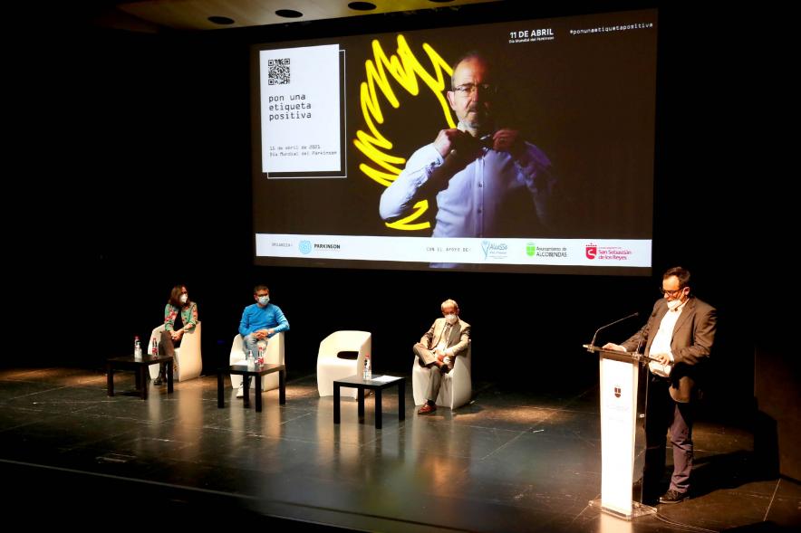 Día Mundial del Parkinson - Imagen lejana de un momento de la intervención  presidente de la FEP Andrés Álvarez y vemos a los otros ponentes en el escenario.