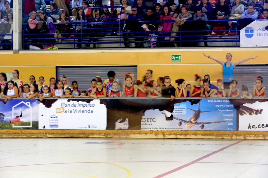 Gala de Patinaje Artístico Virgen de la Paz - Imagen lejana de una entrenadora dando indicaciones a su equipo desde fuera de la pista y la patinadoras otro equipo mirando la actuación.