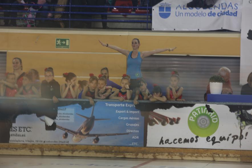 Gala de Patinaje Artístico Virgen de la Paz - Imagen de una entrenadora dando indicaciones a su equipo desde fuera de la pista y la patinadoras otro equipo mirando la actuación.