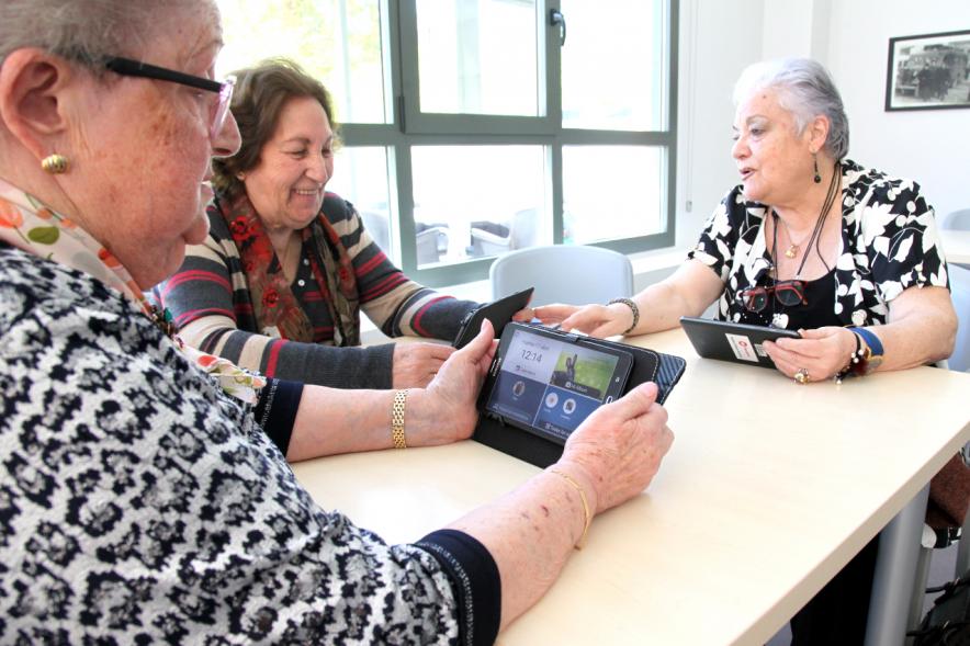 Presentación Proyecto Piloto Familyar Social Service - Imagen de unas personas mayores probando el dispositivo que se esta presentando en el acto.