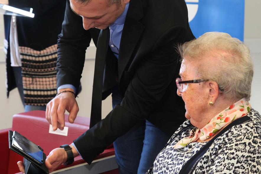 Presentación Proyecto Piloto Familyar Social Service - Imagen de una persona mayor recibiendo el dispositivo que se esta presentando en el acto.