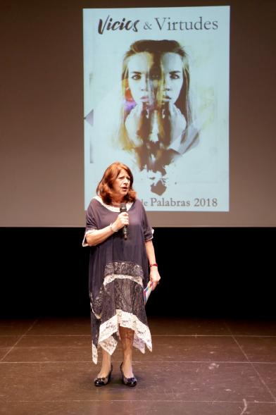Presentación del Libro Sinfonía de Palabras 2018 y Entrega Premio Ganador Certamen MIcrorrelatos - Imagen de la coordinadora en el escenario con el cartel de fondo..