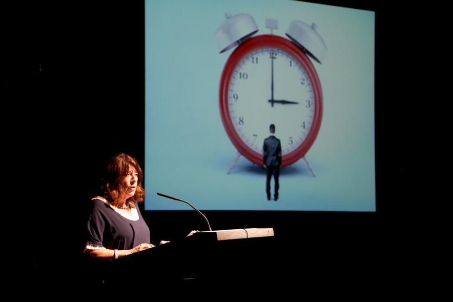 Presentación del Libro Sinfonía de Palabras 2018 y Entrega Premio Ganador Certamen MIcrorrelatos - Imagen de una participante  leyendo  con el cartellde fondo.