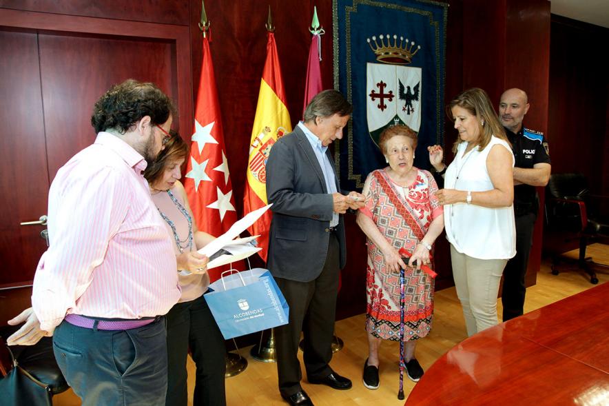 Entrega de Pulseras QR a la Asociación del Alzheimer - Imagen del alcalde García de Vinuesa entregando la pulsera a una mujer en presencia de otras autoridades.