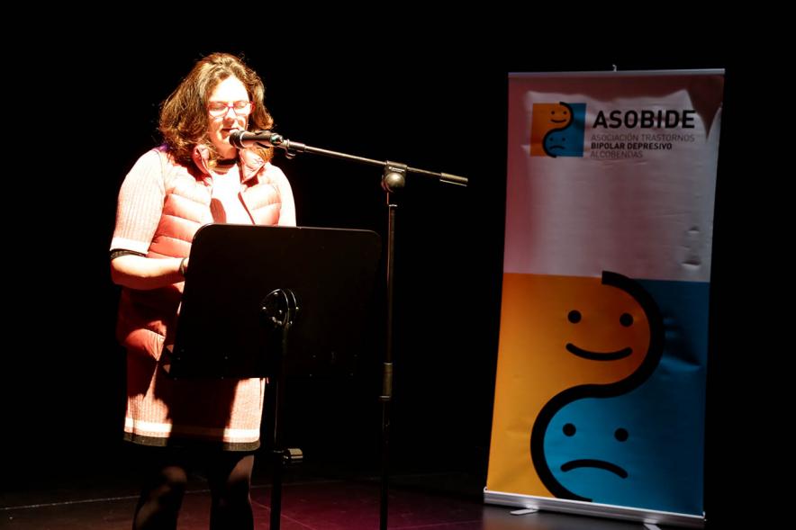 Recital Benéfico de Poesía Mujeres Poetas - Imagen de la poeta recitando con el escenario a media luz.