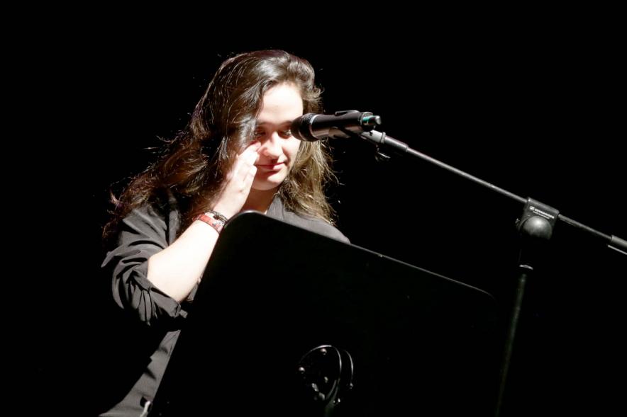 Recital Benéfico de Poesía Mujeres Poetas - Imagen de la poeta recitando con el escenario a media luz.