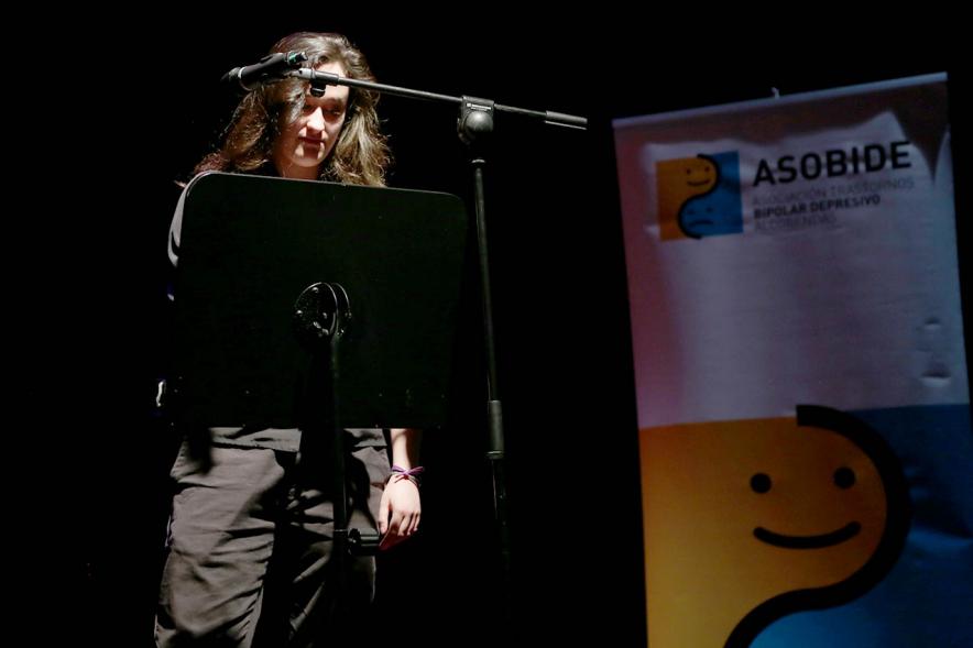 Recital Benéfico de Poesía Mujeres Poetas -  Imagen de la poeta recitando con el escenario a media luz.