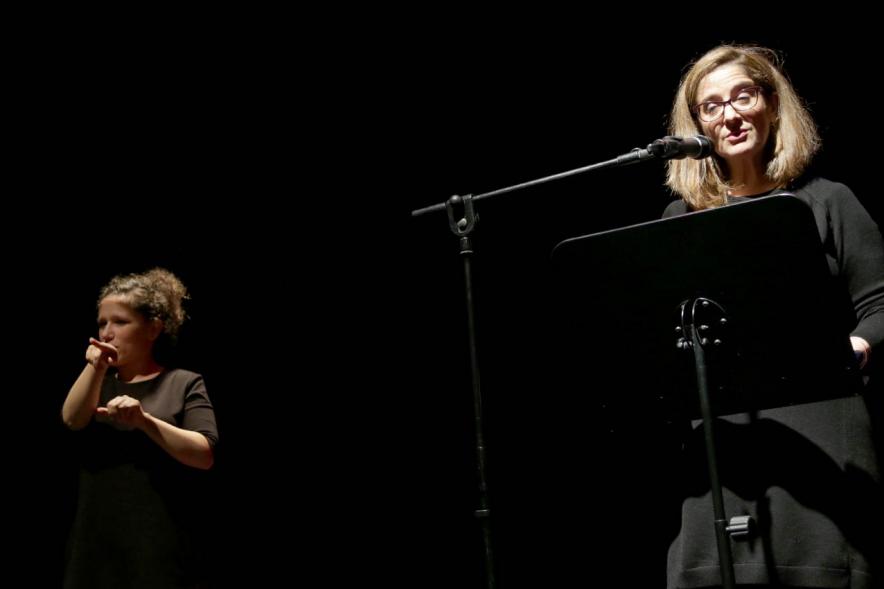 Recital Benéfico de Poesía Mujeres Poetas -  Imagen de Rosa García recitando con el acompañamiento de una flauta.