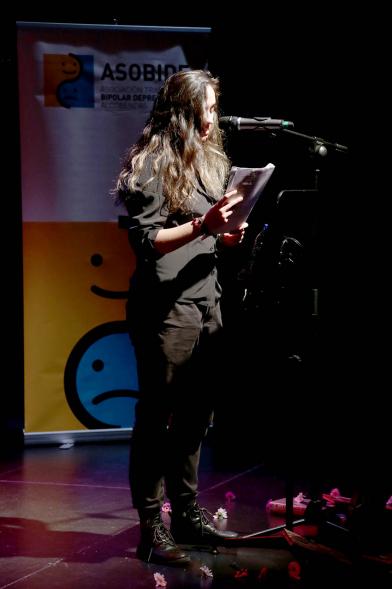 Recital Benéfico de Poesía Mujeres Poetas -  Imagen de la poeta recitando con el escenario a media luz.