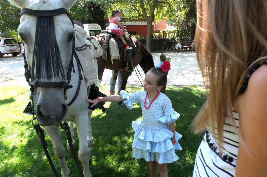 XXIV Romería Andaluza - Imagen de una niña vestida con traje típico andaluz acariciando un caballo.