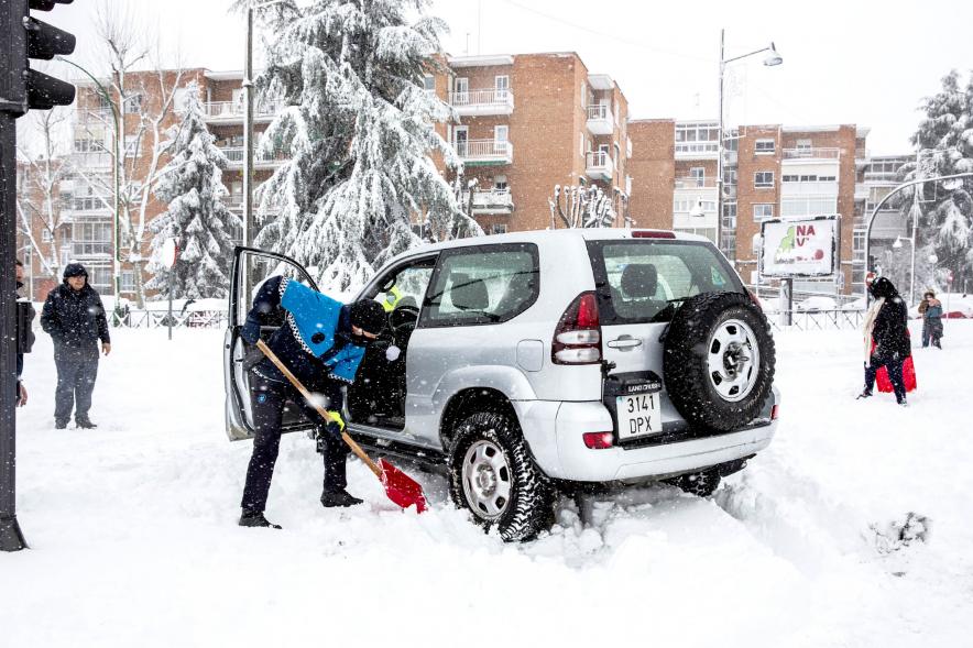 Policía con pala liberando un coche atrapado en la nieve