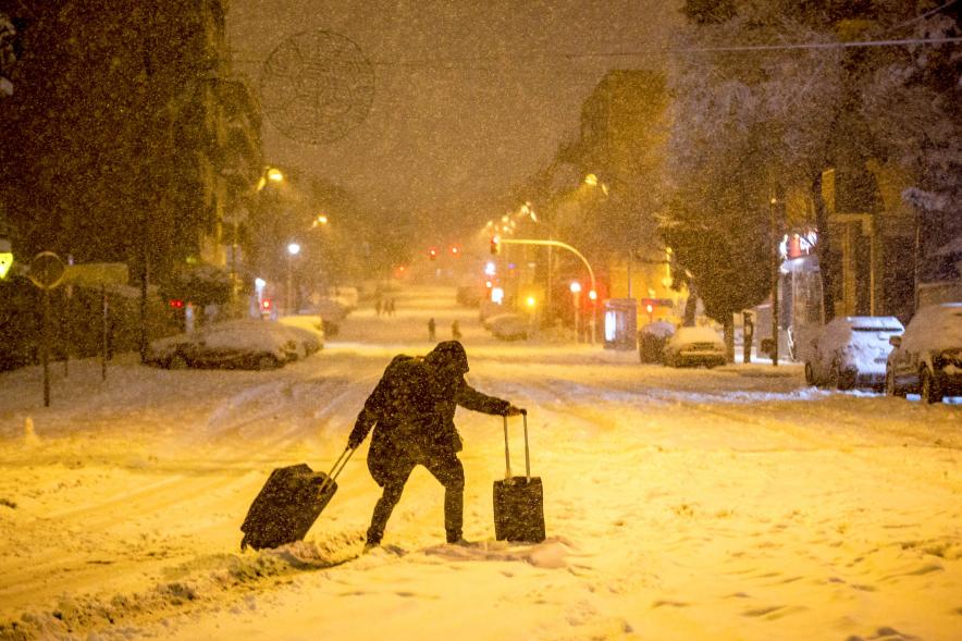 Ciudadano trata de cruzar con maletas una calle bloqueada por la nieve