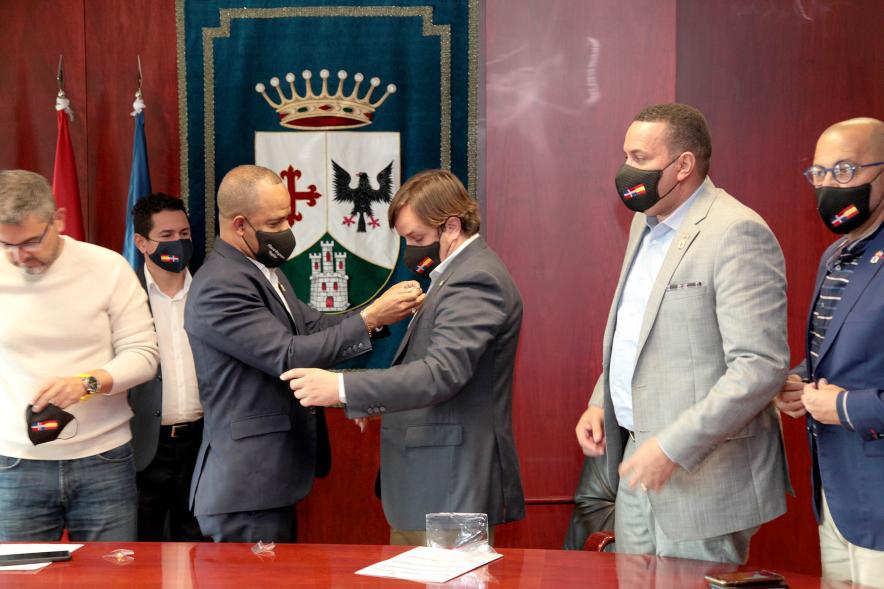 Bienvenida Delegación República Dominicana - Imagen de un miembro de la delegación República Dominicana colocando un insignia a una de las autoridades de Alcobendas.