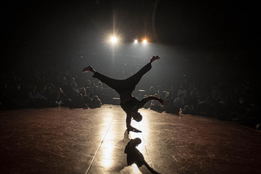 A Ras de Suelo - Breakdance - Imagen a contraluz de un joven realizando un movimiento de Breakdance.