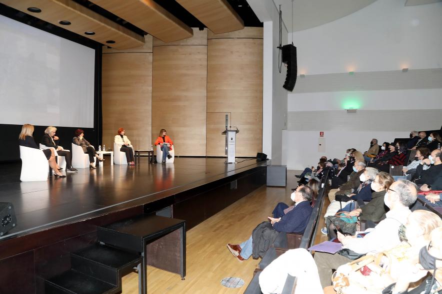 Coloquio y Visita Guiada a la Exposición "Cinco Miradas"  -  Imagen vista panorámica lejana del escenario donde vemos a las participantes en el coloquio.
