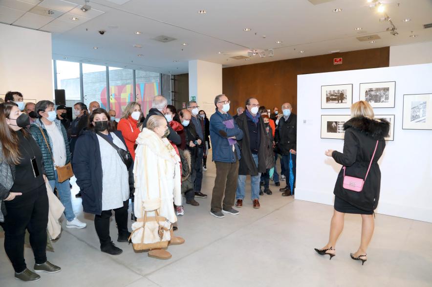 Coloquio y Visita Guiada a la Exposición "Cinco Miradas" - Imagen de la hija de Queca Campillo (Carmen Gutiérrez Campillo) realizando la visita guiada de la obra de su madre incluida en la exposición “Mujeres Reporteras: Cinco Miradas” y parte del público asistente.