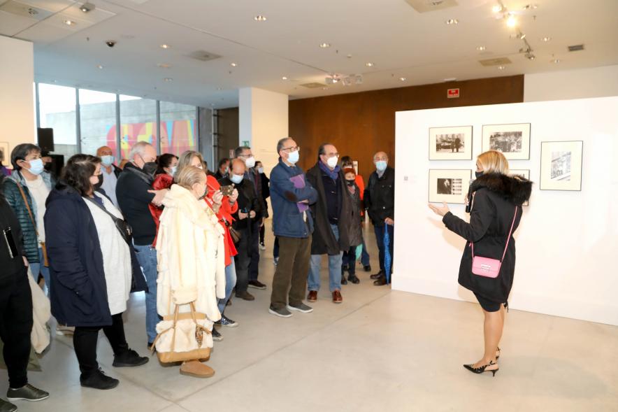 Coloquio y Visita Guiada a la Exposición "Cinco Miradas" - Imagen de la hija de Queca Campillo (Carmen Gutiérrez Campillo) realizando la visita guiada de la obra de su madre incluida en la exposición “Mujeres Reporteras: Cinco Miradas” y parte del público asistente.