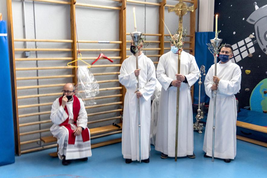 Semana Santa 2022 - Domingo de Ramos -  Imagen de los sacerdotes en el gimnasio donde se celebra una parada de la procesion.
